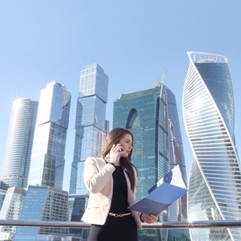 Young beautiful businesswoman with cellphone outdoors at skyscraper background