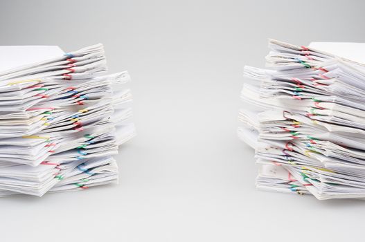 Dual pile overload of document with colorful paper clip place on white table.