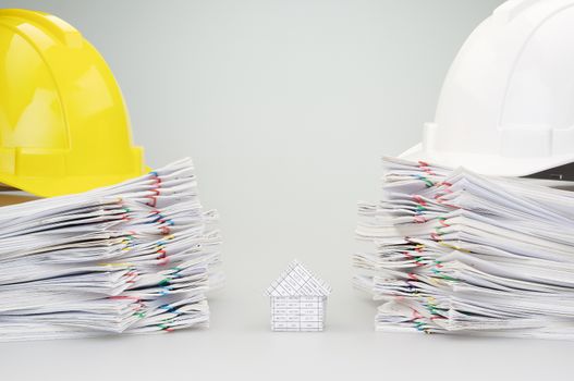 House between pile overload document of report and receipt with colorful paperclip have yellow and white engineer hat on top with white background.