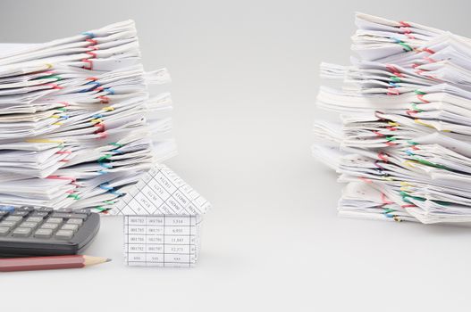 House with pencil and calculator with dual pile overload document of report and receipt with colorful paperclip on white background.