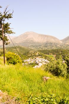 Village Cretan perched on a hill among the olive trees and trees with mountains in the background