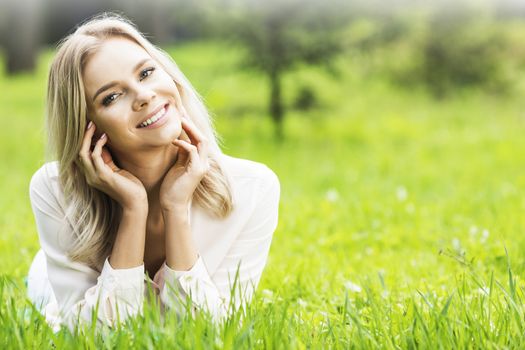 Young attractive blond girl is relaxing in the park laying on grass