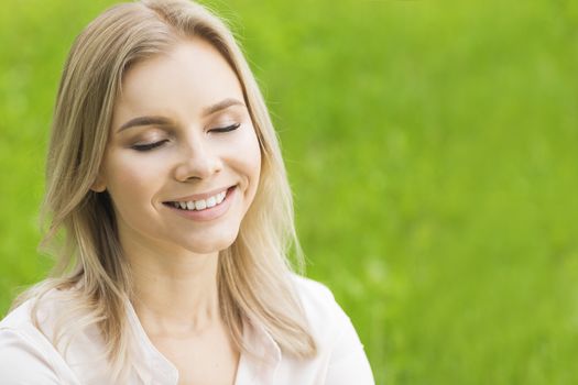 A beautiful young woman on grass enjoy nature smiling with closed eyes