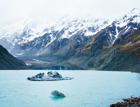 Two irregular icebergs floating in Hooker Lake, New Zealand. Glacier in the background shadowed over by rugged snow capped mountains.