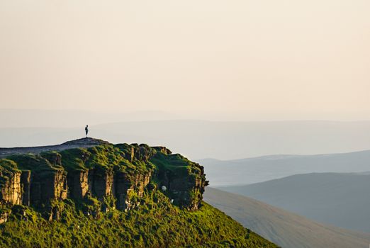 Man standing on a cliff looking out over the valley during sunset. Shot in Brecon Beacon in early summer. Wales