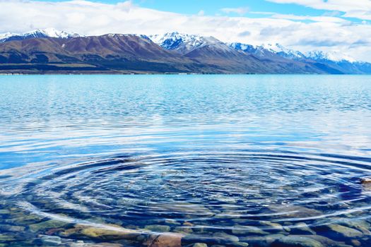 Ripple in water of Lake Pukaki in foreground. Turquoise lake and snow capped mountains in background. New Zealand.