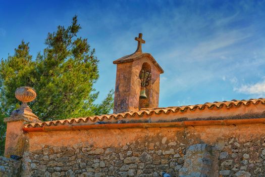 Church tower with bell in Spanish style against a blue sky.