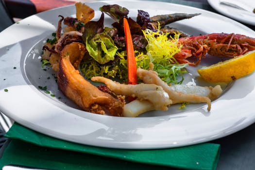 Closeup of various grilled kinds of fish on a white plate in the restaurant.