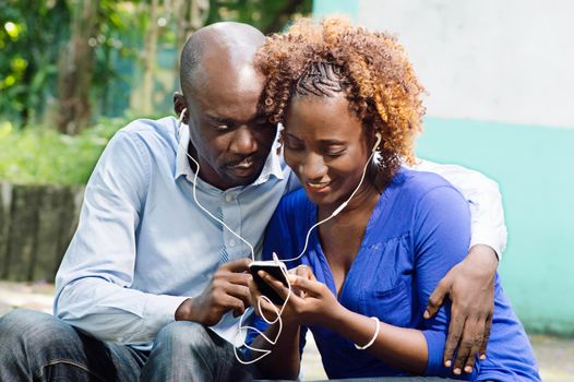 This happy couple sitting in a park and share a common telephone information