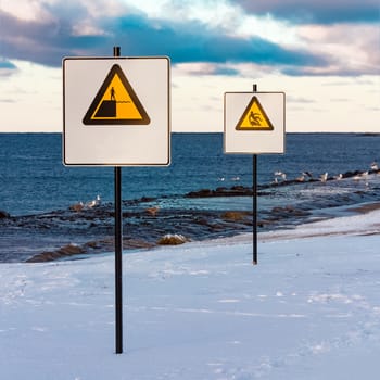 Two yellow warning signs on the winter beach