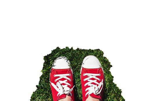 Legs in old red sneakers on green grass. View from above. The concept of youth, spring and freedom. Isolated on white background.