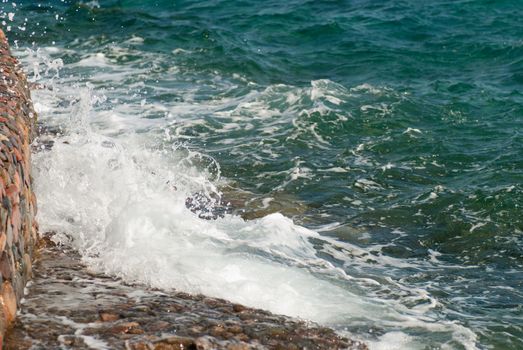 Photo of beautiful clear turquoise sea ocean water surface with ripples and bright splash on stone seascape background, horizontal picture.