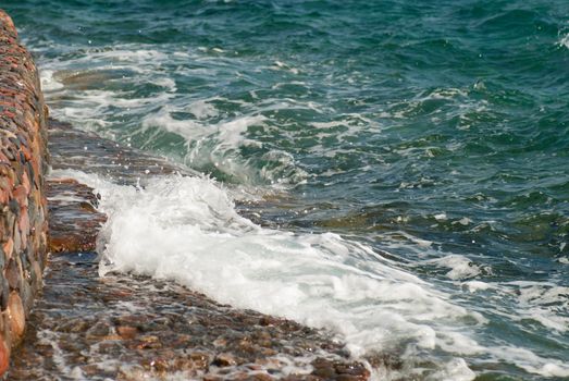 Photo of beautiful clear turquoise sea ocean water surface with ripples and bright splash on stone seascape background, horizontal picture.