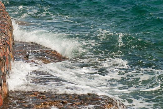 Photo of beautiful clear turquoise sea ocean water surface with ripples and bright splash on stone seascape background, horizontal picture.