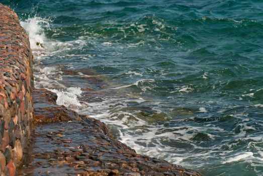 Photo of beautiful clear turquoise sea ocean water surface with ripples and bright splash on stone seascape background, horizontal picture.