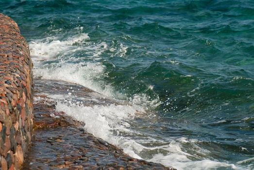 Photo of beautiful clear turquoise sea ocean water surface with ripples and bright splash on stone seascape background, horizontal picture.