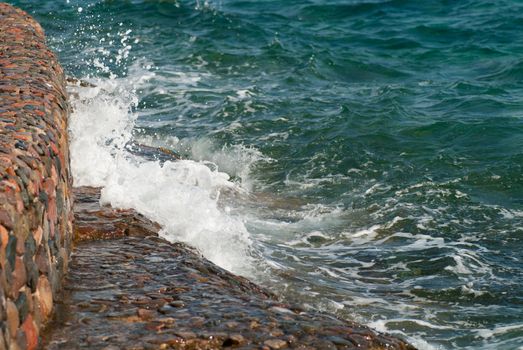 Photo of beautiful clear turquoise sea ocean water surface with ripples and bright splash on stone seascape background, horizontal picture.