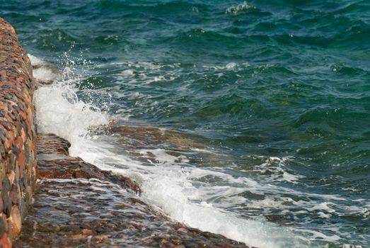 Photo of beautiful clear turquoise sea ocean water surface with ripples and bright splash on stone seascape background, horizontal picture.