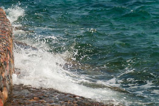 Photo of beautiful clear turquoise sea ocean water surface with ripples and bright splash on stone seascape background, horizontal picture.