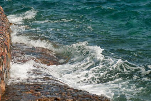 Photo of beautiful clear turquoise sea ocean water surface with ripples and bright splash on stone seascape background, horizontal picture.