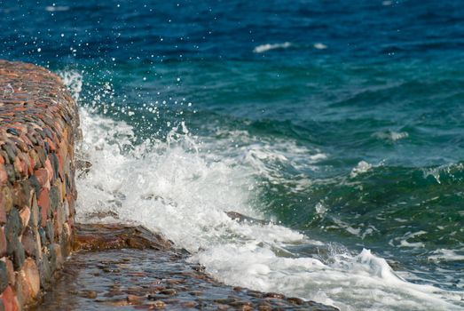 Photo of beautiful clear turquoise sea ocean water surface with ripples and bright splash on stone seascape background, horizontal picture.