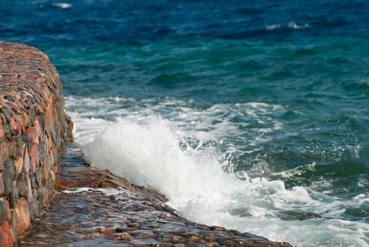 Photo of beautiful clear turquoise sea ocean water surface with ripples and bright splash on stone seascape background, horizontal picture.