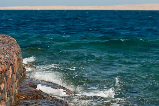 Photo of beautiful clear turquoise sea ocean water surface with ripples and bright splash on stone seascape background, horizontal picture.