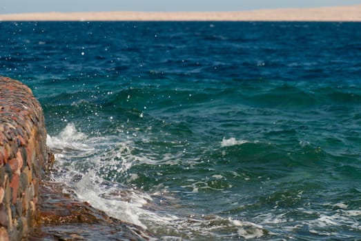 Photo of beautiful clear turquoise sea ocean water surface with ripples and bright splash on stone seascape background, horizontal picture.