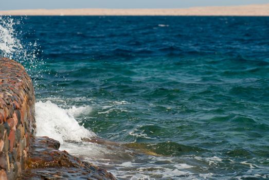 Photo of beautiful clear turquoise sea ocean water surface with ripples and bright splash on stone seascape background, horizontal picture.