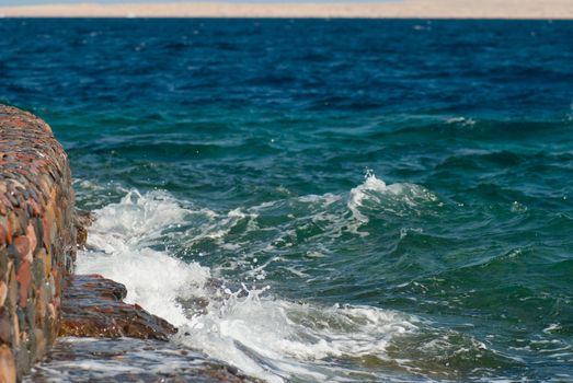 Photo of beautiful clear turquoise sea ocean water surface with ripples and bright splash on stone seascape background, horizontal picture.