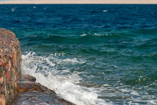 Photo of beautiful clear turquoise sea ocean water surface with ripples and bright splash on stone seascape background, horizontal picture.