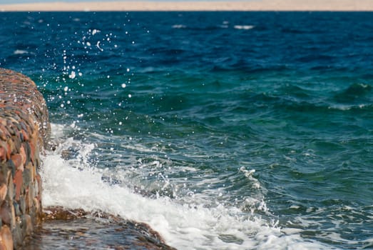 Photo of beautiful clear turquoise sea ocean water surface with ripples and bright splash on stone seascape background, horizontal picture.