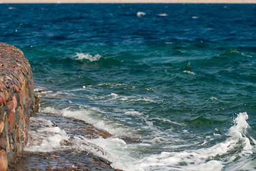 Photo of beautiful clear turquoise sea ocean water surface with ripples and bright splash on stone seascape background, horizontal picture.