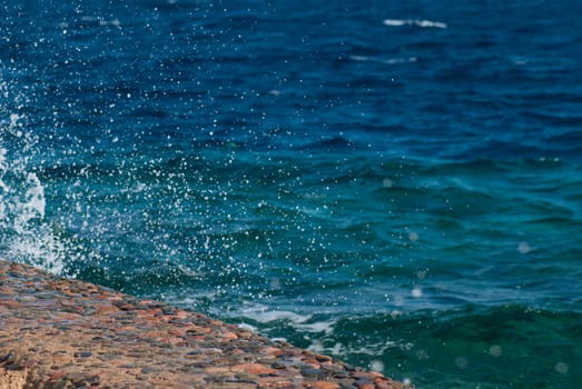 Photo of beautiful clear turquoise sea ocean water surface with ripples and bright splash on stone seascape background, horizontal picture.