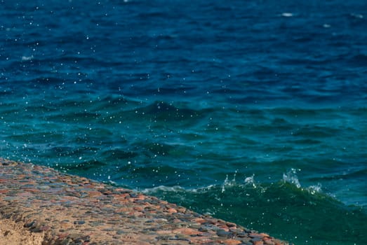 Photo of beautiful clear turquoise sea ocean water surface with ripples and bright splash on stone seascape background, horizontal picture.