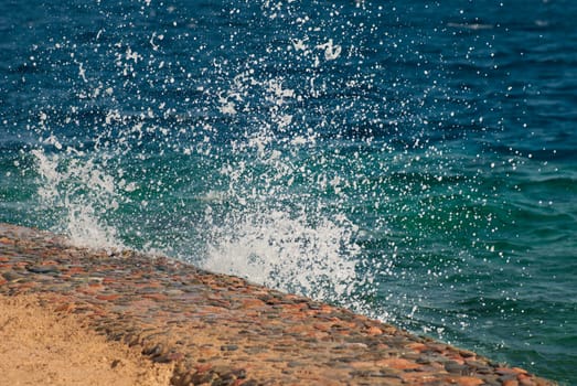 Photo of beautiful clear turquoise sea ocean water surface with ripples and bright splash on stone seascape background, horizontal picture.