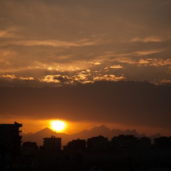 Sunset at city of Hurghada with buildings and mountains silhouette.