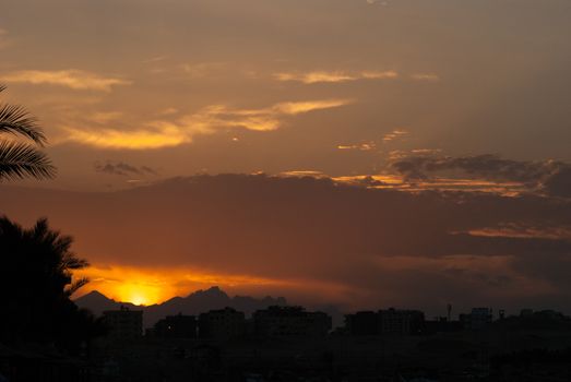 Sunset at city of Hurghada with buildings and mountains silhouette.