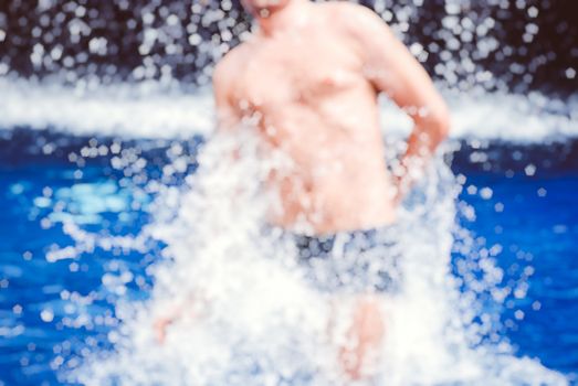 Handsome muscular guy jumping from water blurred bokeh background.