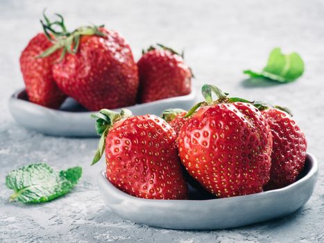 Fresh ripe strawberries in small trendy plate. Strawberry in gray plate and mint leaves on gray concrete background