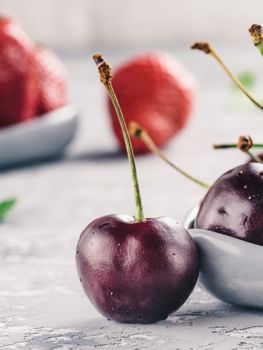 Close up view of fresh ripe cherry. Strawberry on background. Gray concrete table