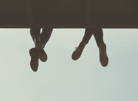 Taking things easy. Two young woman rest their legs over the edge of a balcony.