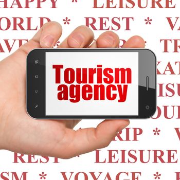 Tourism concept: Hand Holding Smartphone with  red text Tourism Agency on display,  Tag Cloud background, 3D rendering