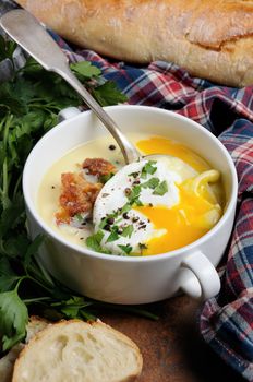 Garlic potato cream soup with bacon and poached eggs, herbs, spices
