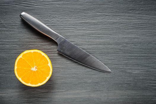 One slice of fresh orange and knife on dark shale background, copyspace