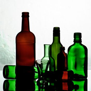 Arrangement of Various Empty Wine Colored Bottles and Glasses with Reflection on Mirror and Shadow Toned Backlight