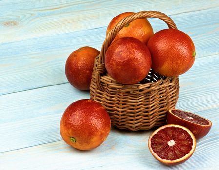 Arrangement of Blood Oranges Full Body and Halves in Wicker Basket closeup on Blue Wooden background
