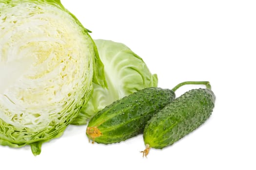 Fragment of the head of the young fresh white cabbage cut in half against of second half of cabbage and two fresh cucumbers on a light background
