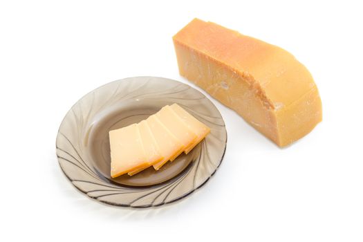 Several thin slices of the Dutch hard cheese Beemster on a dark glass saucer and piece of the same cheese beside on a light background
