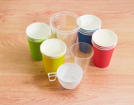 Different disposable transparent and white plastic cups, piles of the disposable paper cups in red, green, blue and yellow colors on a wooden surface
